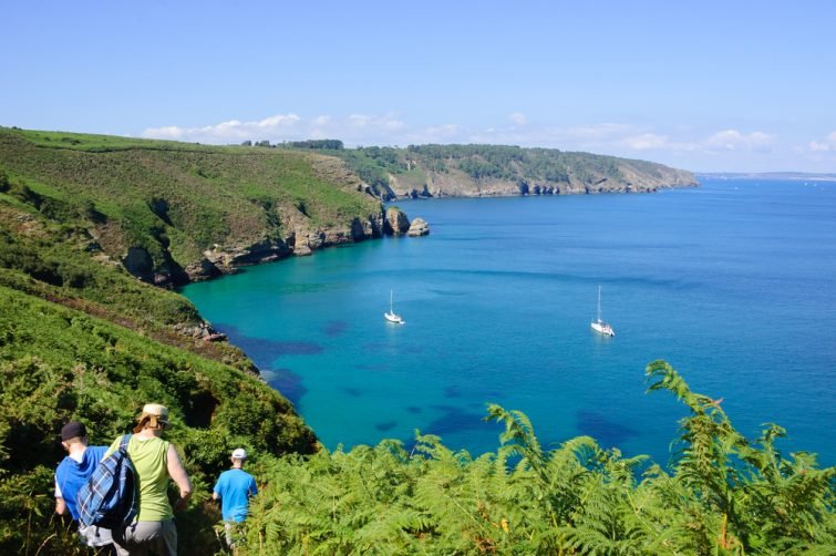 Des touristes randonnant sur les collines près du Cap de la Chevre avec une belle vue sur une baie avec voiliers blancs. Bretagne, France. Arrière-plan vacances en famille actif.