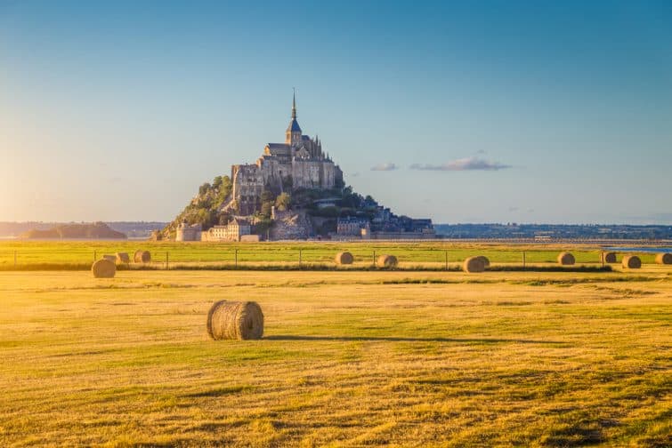 Belle vue sur l'île de marée du Mont Saint-Michel, belle lumière dorée le soir au coucher du soleil en été avec des balles de foin sur les champs vides, Normandie, Nord de la France